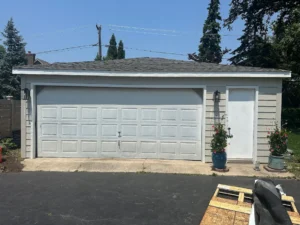 Detached garage with a white 2-car door, side entry door, and potted plants on the right.