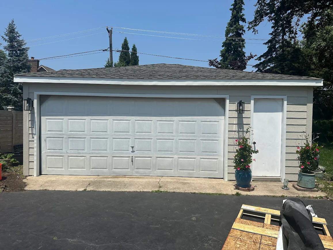 Detached garage with a white 2-car door, side entry door, and potted plants on the right.