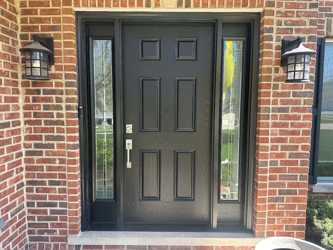 Black paneled front door with narrow glass sidelights flanked by brick walls and two outdoor lanterns.