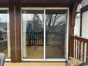 Sliding glass patio door on a wooden deck; a blue ladder is visible inside. Outside railing and a power cord run along the right side.
