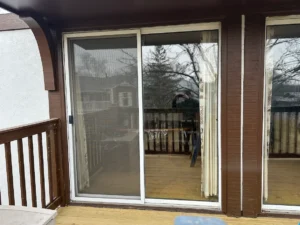Sliding glass door on a wood-deck balcony, with the photographer visible in the reflection of the glass