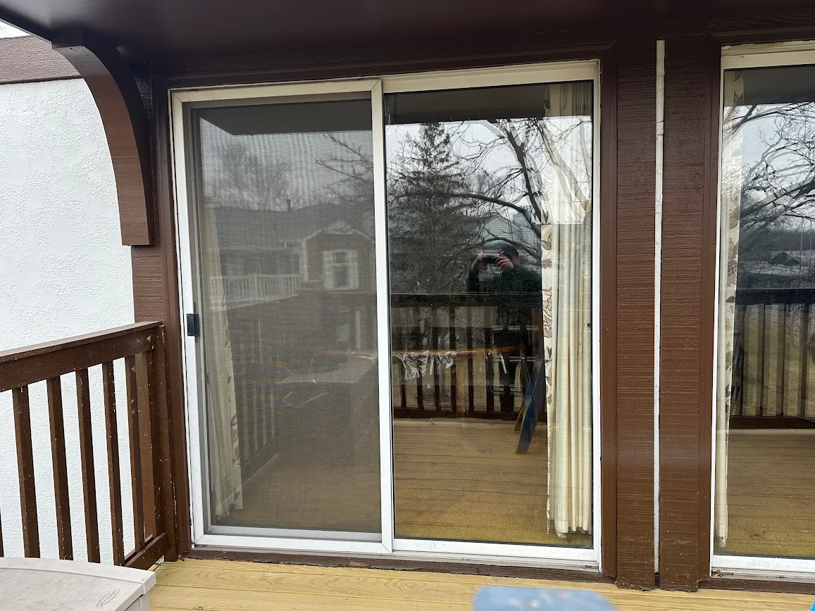 Sliding glass door on a wood-deck balcony, with the photographer visible in the reflection of the glass